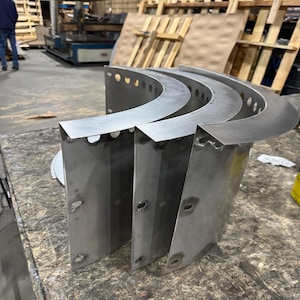 May include: Three curved, silver-colored metal panels with a smooth finish. Each panel features a wide, flat top flange with a series of evenly spaced circular holes along the edge and vertical side sections with additional punched slots.