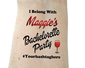 May include: Temporary tattoo with the text "I Belong With Maggie's Bachelorette Party #Yourhashtag here" in black and red lettering. A glass of red wine is pictured next to the text.