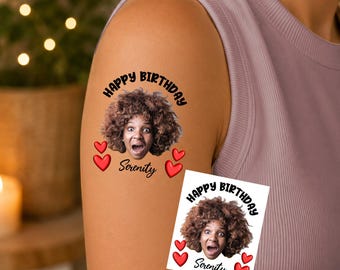 May include: A temporary tattoo applied to skin and a matching square paper sheet, both featuring a photographic portrait of a person with curly brown hair, the text HAPPY BIRTHDAY and Serenity, and four red heart icons arranged around the portrait.