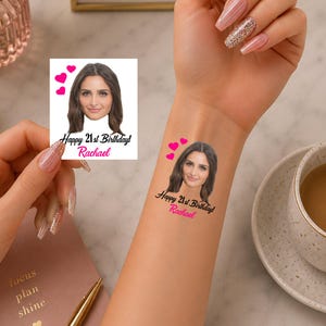 May include: A temporary tattoo featuring a portrait of a person with brown hair, three pink hearts, and the black text Happy 21st Birthday above the pink name Rachael. The design is shown on a square white backing and applied to a forearm.