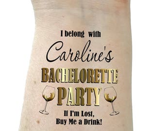 May include: A temporary tattoo with gold lettering that says "I belong with Caroline's Bachelorette Party. If I'm Lost, Buy Me a Drink!" with two gold wine glass silhouettes.