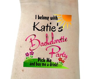 May include: A temporary tattoo with the text "I belong with Katie's Bachelorette Party." The design includes a sun, flowers, and the phrase "Pick Me and buy me a drink!" in a playful font.