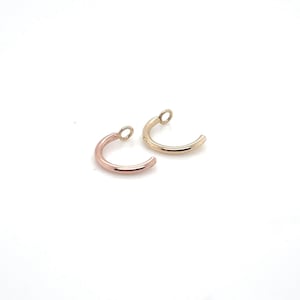 May include: Two small hoop earrings, one gold and one rose gold. Both have a small loop at the top for attaching to a chain or other jewelry.