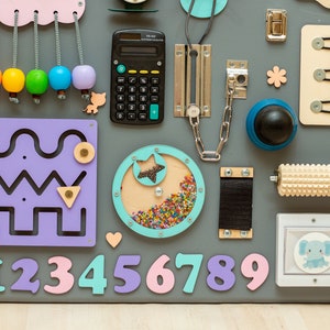 May include: A colorful wooden activity board for toddlers with a variety of textures and activities, including a calculator, a chain, a rolling pin, a lock, a maze, a star-shaped spinner, buttons, and numbers 0-9.