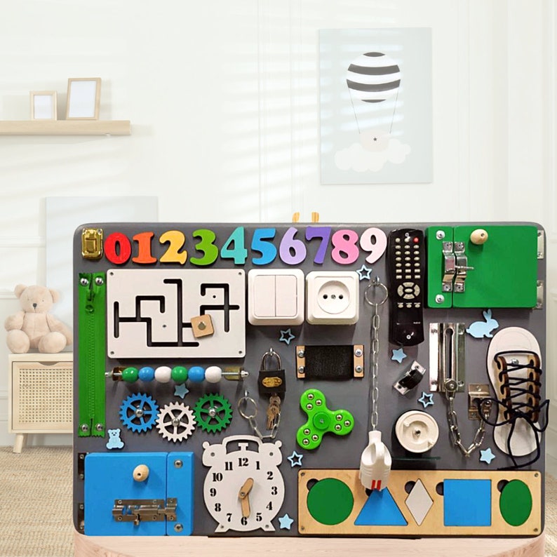 May include: A gray wooden activity board for toddlers with various textures and activities, including a zipper, a lock, a light switch, an outlet, a clock, a maze, gears, a chain, a key, a spinner, a shoe, a remote control, and a rabbit. The numbers 0-9 are displayed at the top of the board.