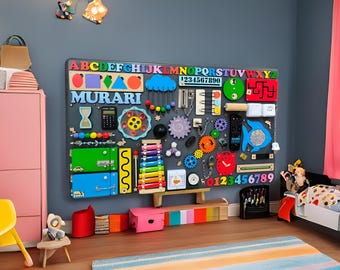 Könnte beinhalten: Ein farbenfrohes Holz-Aktivitätsbrett mit Buchstaben, Zahlen, Formen und anderen interaktiven Elementen. Das Brett ist an einer Wand montiert und trägt eine Namensschilder mit der Aufschrift "MURARI".