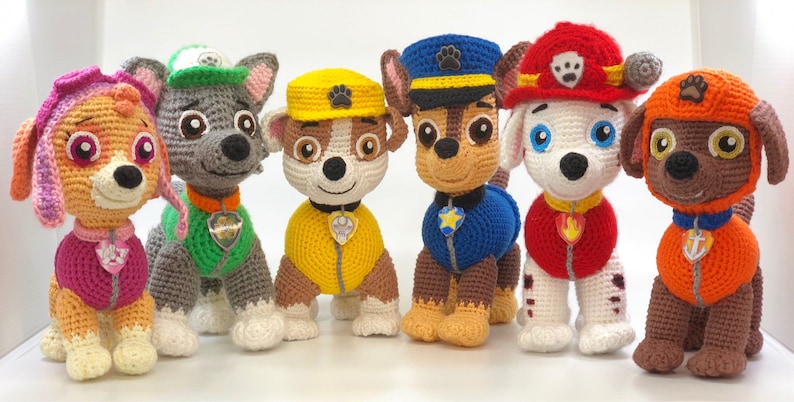Op de afbeelding: Zes gehaakte pluche speelgoed van de Paw Patrol-karakters. De karakters zijn Chase, Marshall, Skye, Rocky, Zuma en Rubble. Elk karakter draagt zijn kenmerkende uniform en hoed.