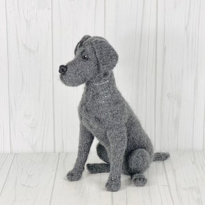 Puede incluir: Un juguete de perro de punto gris en posici&oacute;n sentada. El juguete tiene un aspecto realista con un cuerpo de punto gris y una nariz negra.