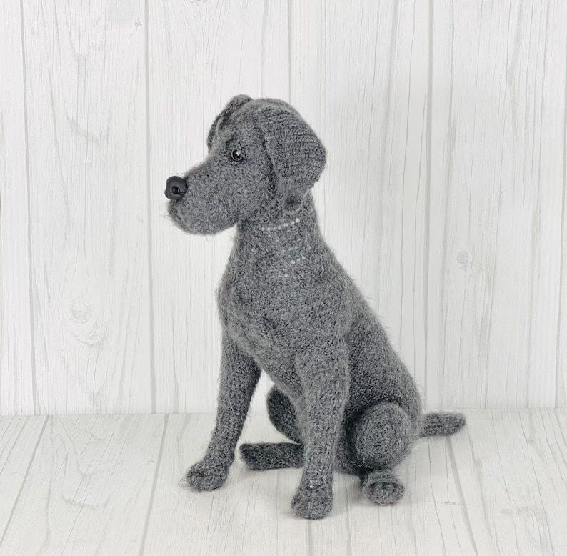 Puede incluir: Un juguete de perro de punto gris en posici&oacute;n sentada. El juguete tiene un aspecto realista con un cuerpo de punto gris y una nariz negra.