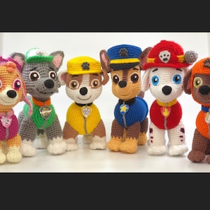Op de afbeelding: Zeven gehaakte pluche speelgoed van de Paw Patrol-personages. De personages zijn Chase, Marshall, Skye, Rocky, Zuma, Rubble en Everest. De speelgoedjes dragen allemaal hun kenmerkende uniformen en accessoires.