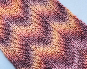 May include: Close-up of a knitted fabric with a textured pattern in shades of orange, pink, and brown.