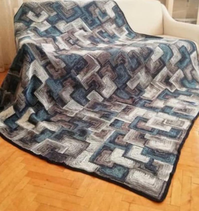 May include: A crocheted throw blanket with a geometric pattern in shades of blue, gray, and white. The blanket is draped over a couch.