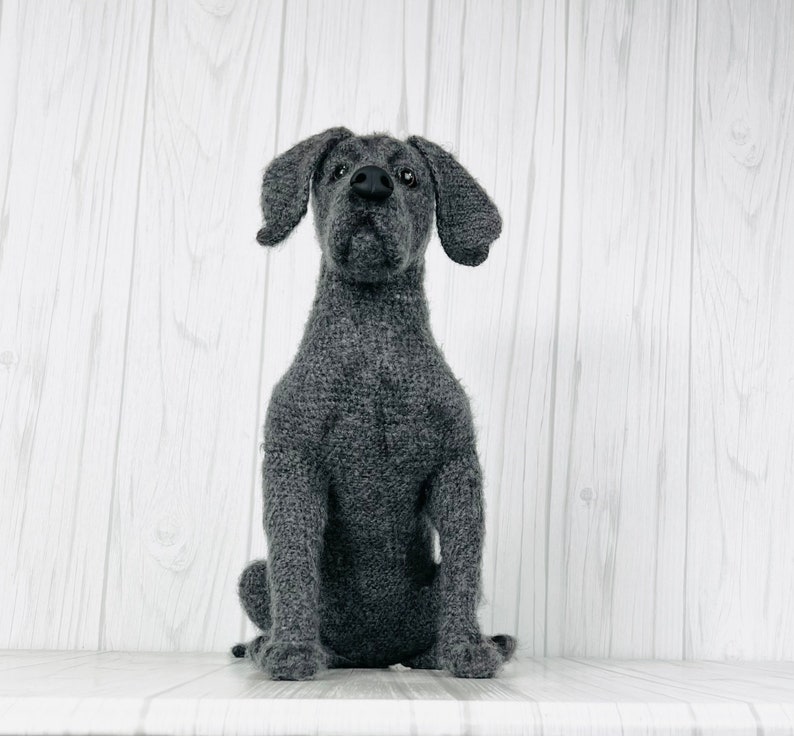 Puede incluir: Un juguete de perro de punto gris con nariz y ojos negros. El juguete est&aacute; sentado sobre una superficie de madera blanca.