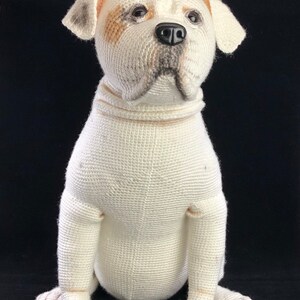 May include: White crocheted stuffed dog sitting with its paws crossed. The dog has brown and black markings on its face.