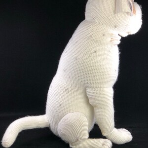 May include: White crocheted plush dog toy sitting on a black background. The dog is sitting with its tail curled behind it.