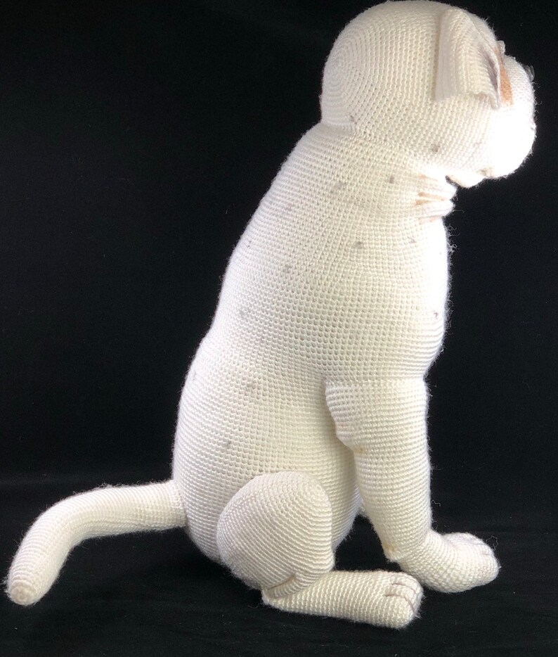 May include: White crocheted plush dog toy sitting on a black background. The dog is sitting with its tail curled behind it.