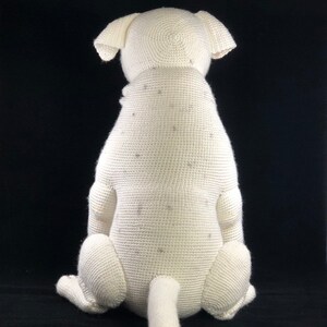 May include: White crocheted dog sitting with its tail curled behind it. The dog is made of white yarn and has a textured surface.
