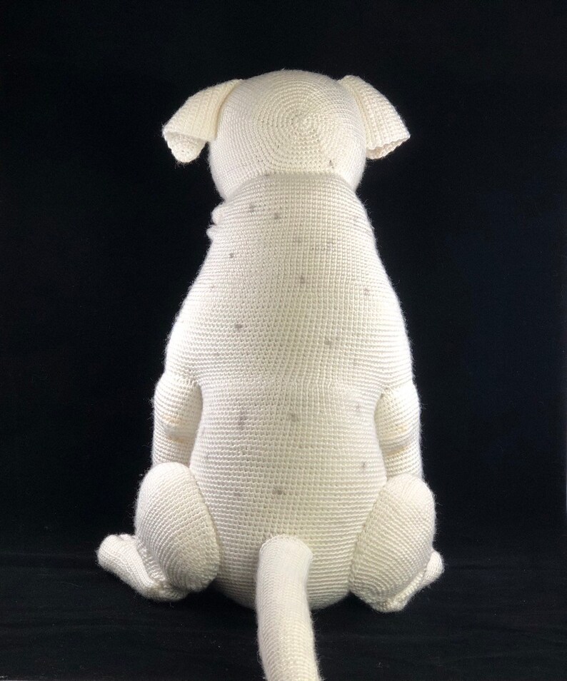 May include: White crocheted dog sitting with its tail curled behind it. The dog is made of white yarn and has a textured surface.