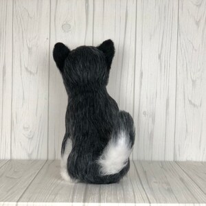 May include: A black and white plush dog toy sitting on a white wooden shelf. The dog is facing away from the camera with its tail curled up.
