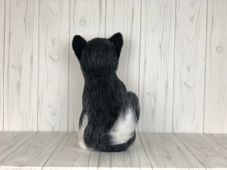 May include: A black and white plush dog toy sitting on a white wooden shelf. The dog is facing away from the camera with its tail curled up.