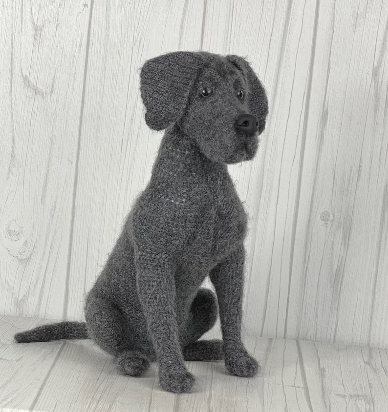 Puede incluir: Un juguete de perro de punto gris en forma de Labrador Retriever. El juguete tiene un aspecto realista con una cara detallada y orejas ca&iacute;das.