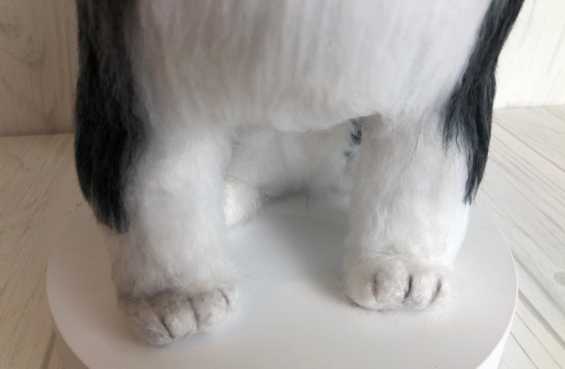 May include: Close-up of a white and black plush dog toy with black fur around the face and ears. The dog is sitting with its paws visible.