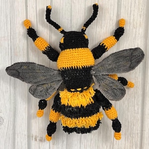 May include: A crocheted bumble bee toy with black and yellow stripes, fuzzy yellow accents, and gray wings.