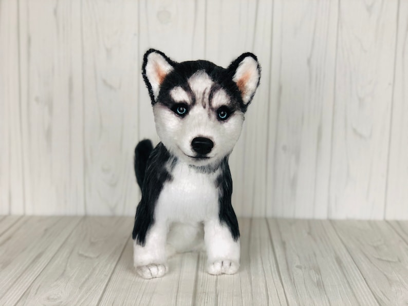 May include: A black and white plush husky puppy toy with blue eyes. The toy is sitting on a white wooden surface.