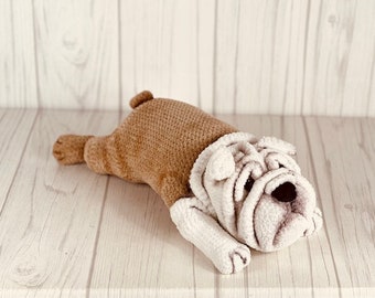 May include: A crocheted stuffed bulldog toy with brown and white fur, lying on a light wood surface.