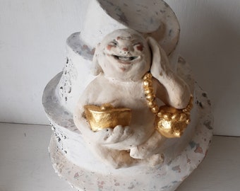 Laughing Buddha sculpture, white ceramic figure with auspicious gold objects on spiral plinth, Buddhist deity