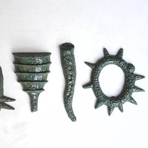 May include: Five ceramic sculptures in a green glaze. The sculptures are abstract and have different shapes, including a rocket, a cone, a horn, a ring with spikes, and a foot.