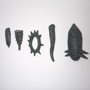 May include: Six small ceramic sculptures in various shapes, including a cone, a ring, a spike, and a long, thin shape. The sculptures are all a dark blue-green color.