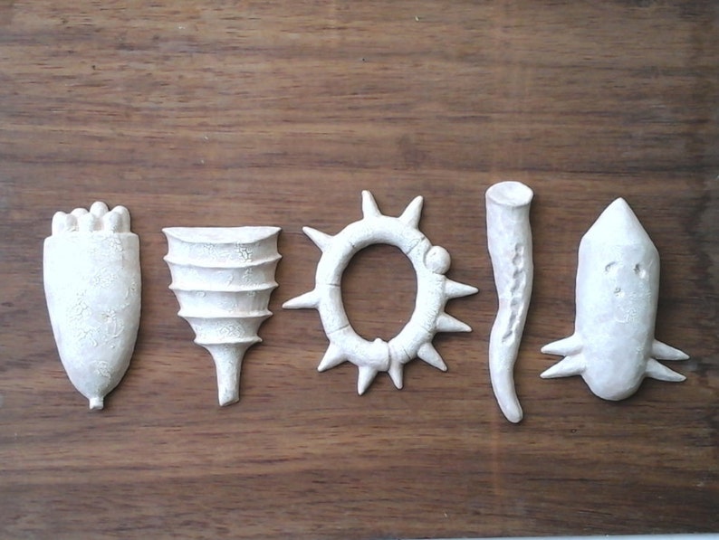 May include: Five white ceramic sculptures with different shapes and textures. The sculptures are arranged in a row on a wooden surface.