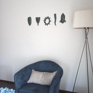 May include: A blue armchair with a white pillow sits in front of a white wall with six decorative wall hangings. A floor lamp with a white shade stands to the right of the chair.