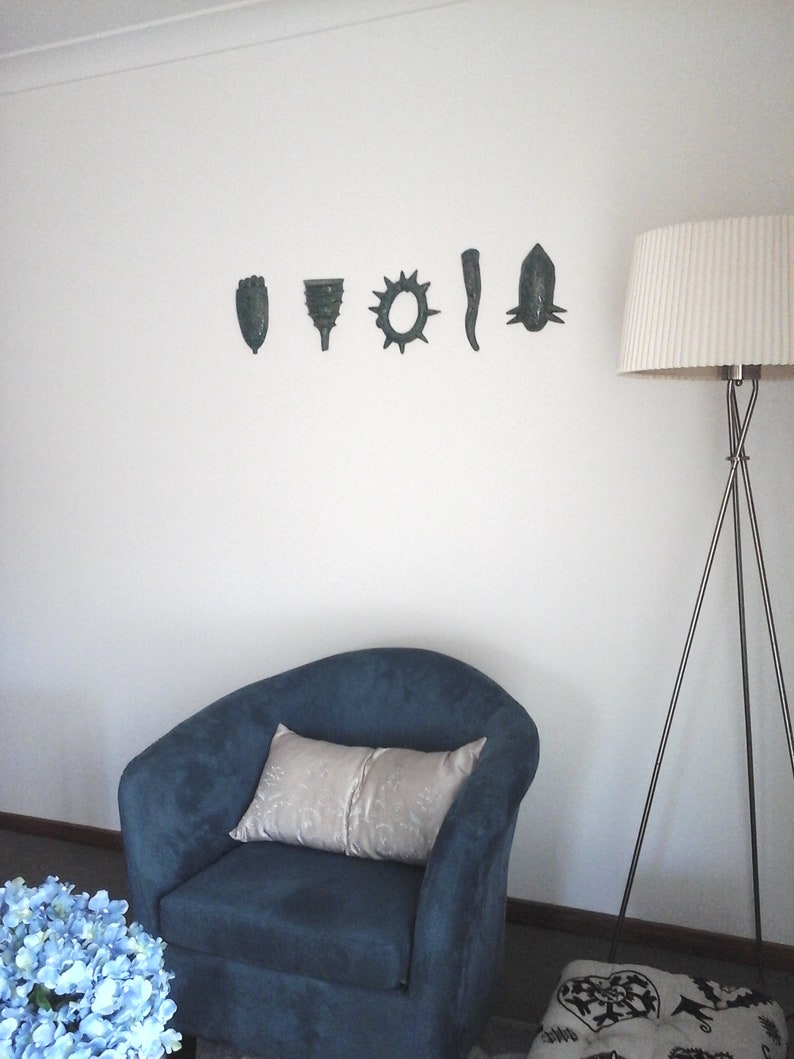 May include: A blue armchair with a white pillow sits in front of a white wall with six decorative wall hangings. A floor lamp with a white shade stands to the right of the chair.