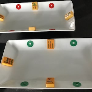 May include: Two white rectangular serving trays with green and red circular designs. The trays are decorated with small yellow and brown tiles with Chinese characters and numbers.