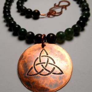 May include: A copper necklace with a Celtic knot pendant and a dark green bead chain.