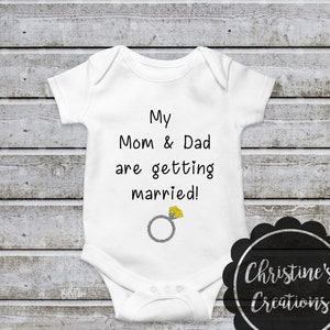 May include: White baby onesie with black text that reads "My Mom & Dad are getting married!" with a silver ring and yellow diamond graphic.