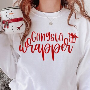 May include: White sweatshirt with red text that says "Gangsta Wrapper" and a small red gift box graphic.