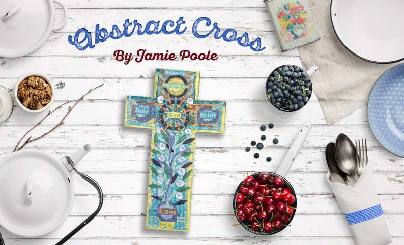 Puede incluir: Una cruz abstracta azul y amarilla con las palabras "Yo soy Jes&uacute;s", "Santo", "Dios", "Esp&iacute;ritu" y "Cielo" en ella. La cruz est&aacute; sobre un fondo de madera blanca con varios cuencos de fruta y otros art&iacute;culos.
