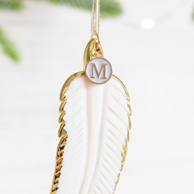 May include: Gold and white feather ornament with a gold circle charm with the letter "M" on it.