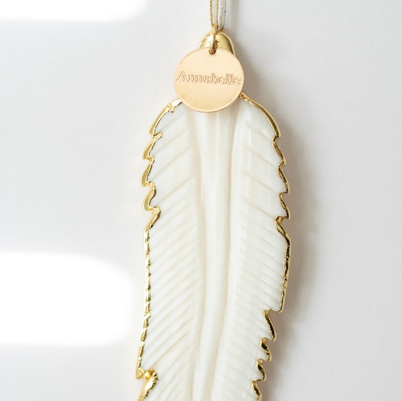 May include: White feather ornament with a gold trim and a gold tag that says "Annabelle".