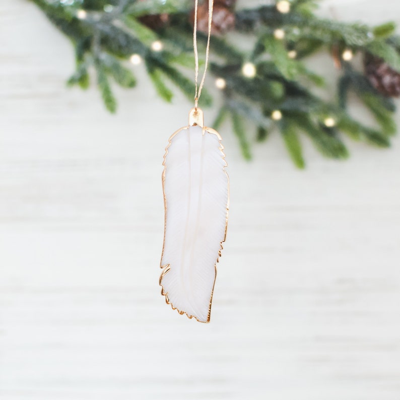 May include: White feather Christmas ornament with a gold outline. The ornament is hanging from a string.