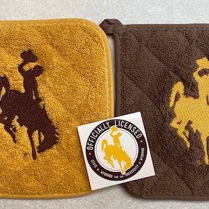 May include: Two square pot holders, one mustard yellow and one brown, each embroidered with a brown and yellow bucking bronco logo. An "Officially Licensed" sticker is placed between them. The pot holders have a loop for hanging.