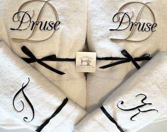 May include: White bath towels with embroidered initials and names. The towels are tied with black satin ribbons. The name "Druse" is embroidered in gold thread on two towels. The other two towels have embroidered initials in black thread.