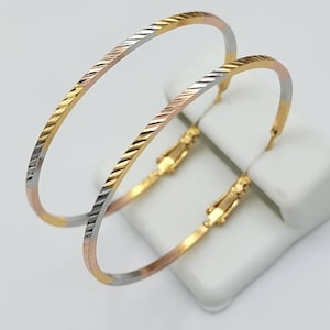 May include: A pair of gold hoop earrings with a textured design. The earrings are made of three different shades of gold: yellow, rose, and white.