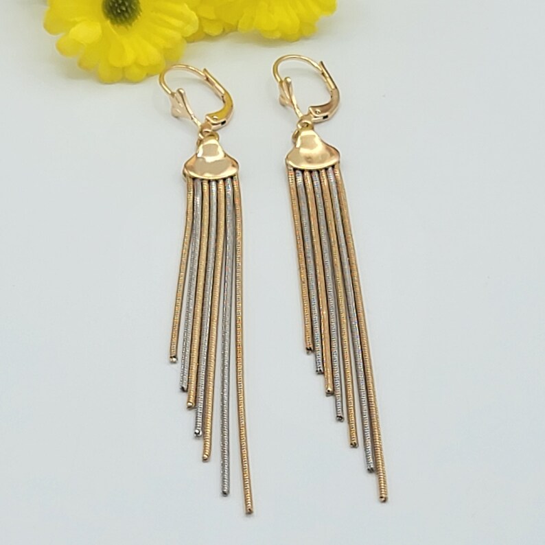 May include: A pair of gold and silver dangle earrings with a chain-like design. The earrings are made of two different metals, one gold and one silver, and are connected by a small loop at the top. The earrings are long and have a delicate, feminine look.