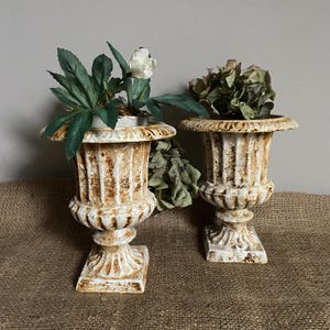 May include: A white ceramic mug with a black handle and the text "But First, Coffee" in a black, bold font. The mug is on a white surface.