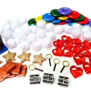 May include: A collection of craft supplies including gold stars, red heart-shaped beads, miniature books, treasure chests, magnifying glasses, and colorful buttons. White fluffy pom-poms and a miniature archway are also included.