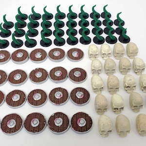 May include: A collection of miniature game pieces, including green tentacles, brown shields, and white skulls. The pieces are arranged in rows on a white surface.